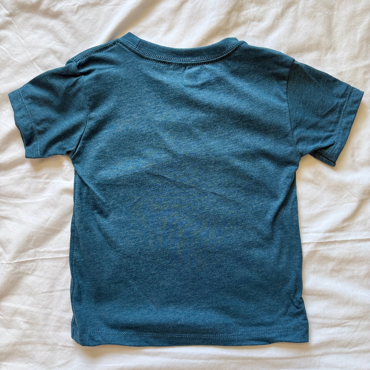 A short-sleeve crewneck t-shirt in a heathered teal blue color, laid flat on a wrinkled white sheet.