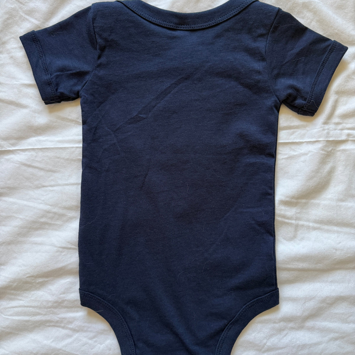 A navy blue short-sleeve baby bodysuit laid flat on a white fabric background.
