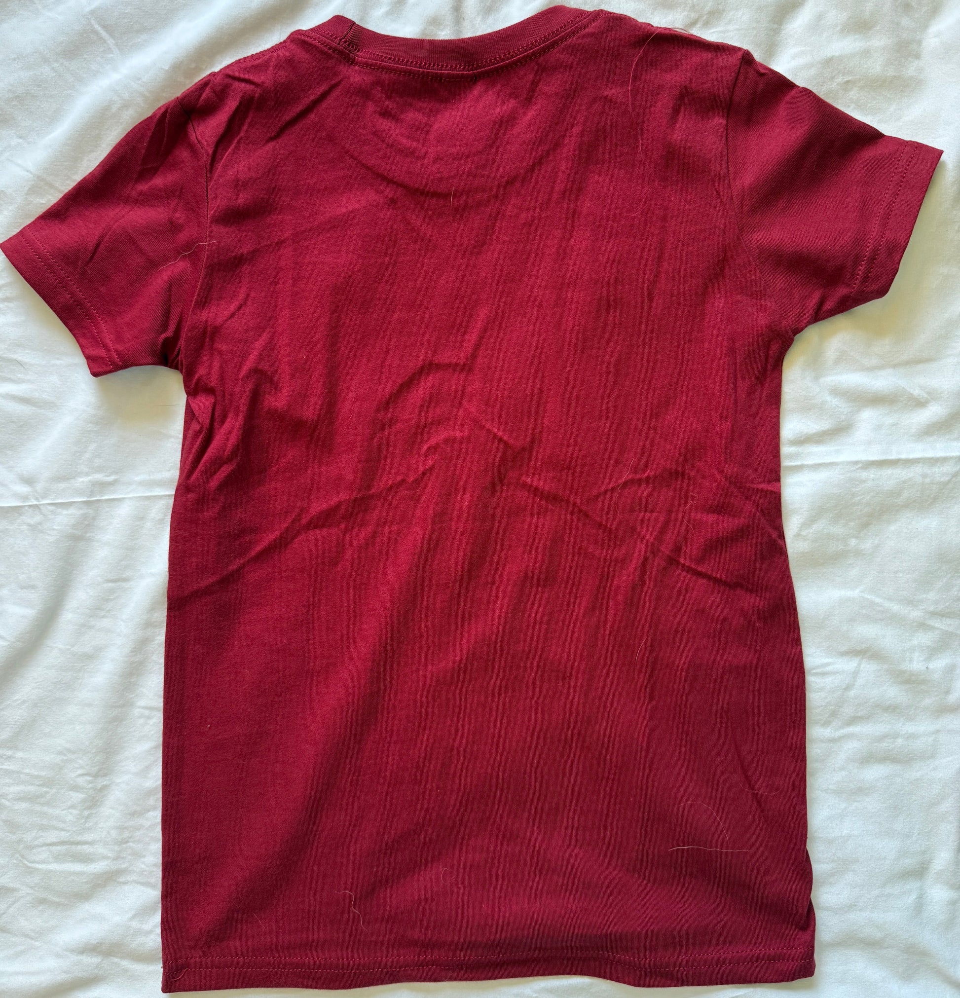 A dark red short-sleeve t-shirt laid flat on a wrinkled white sheet.