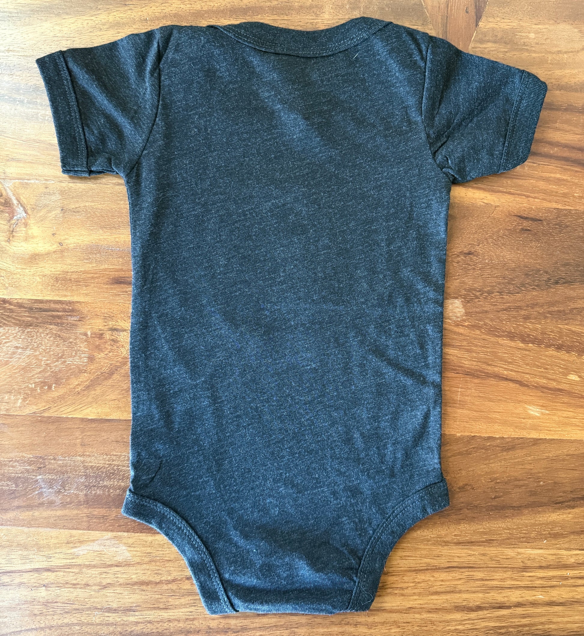 A dark charcoal gray short-sleeve baby bodysuit laid flat on a wooden table.