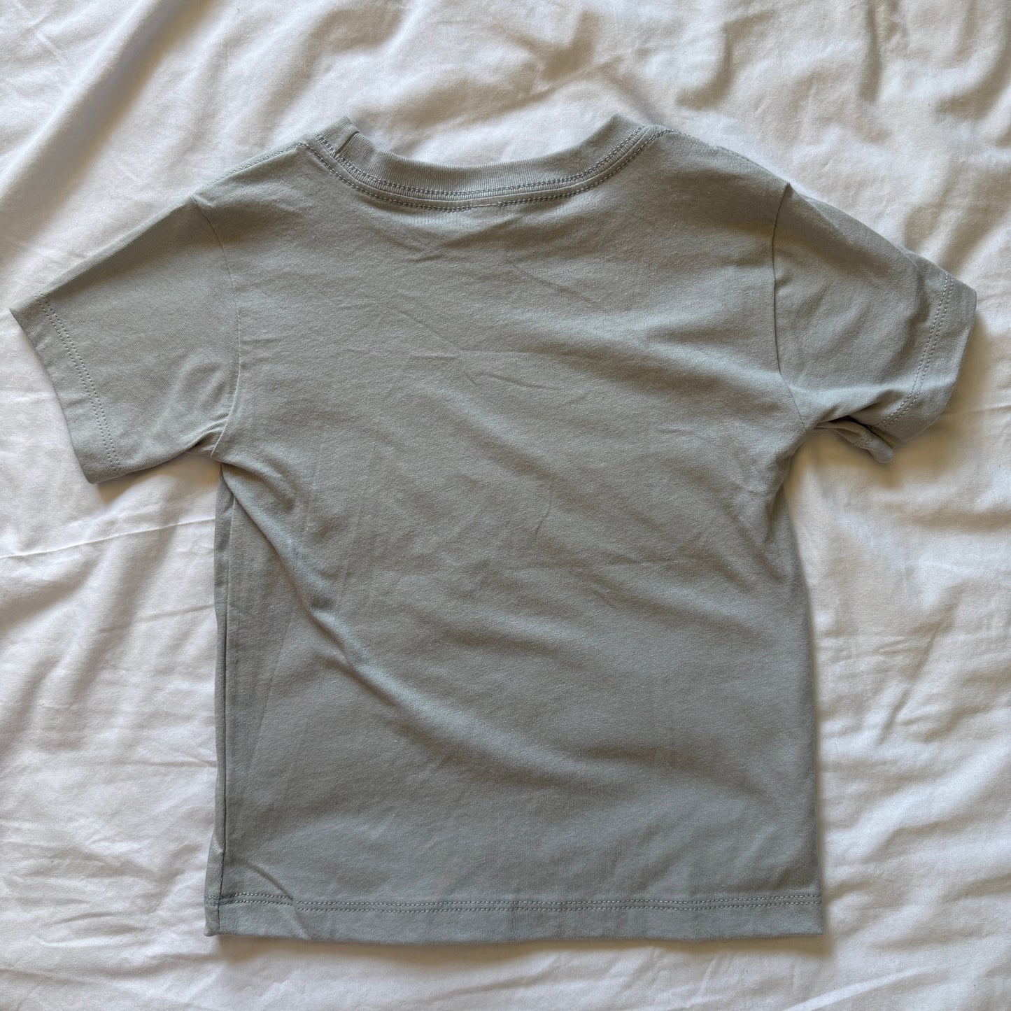 A light gray short-sleeve t-shirt laid flat on a wrinkled white sheet.