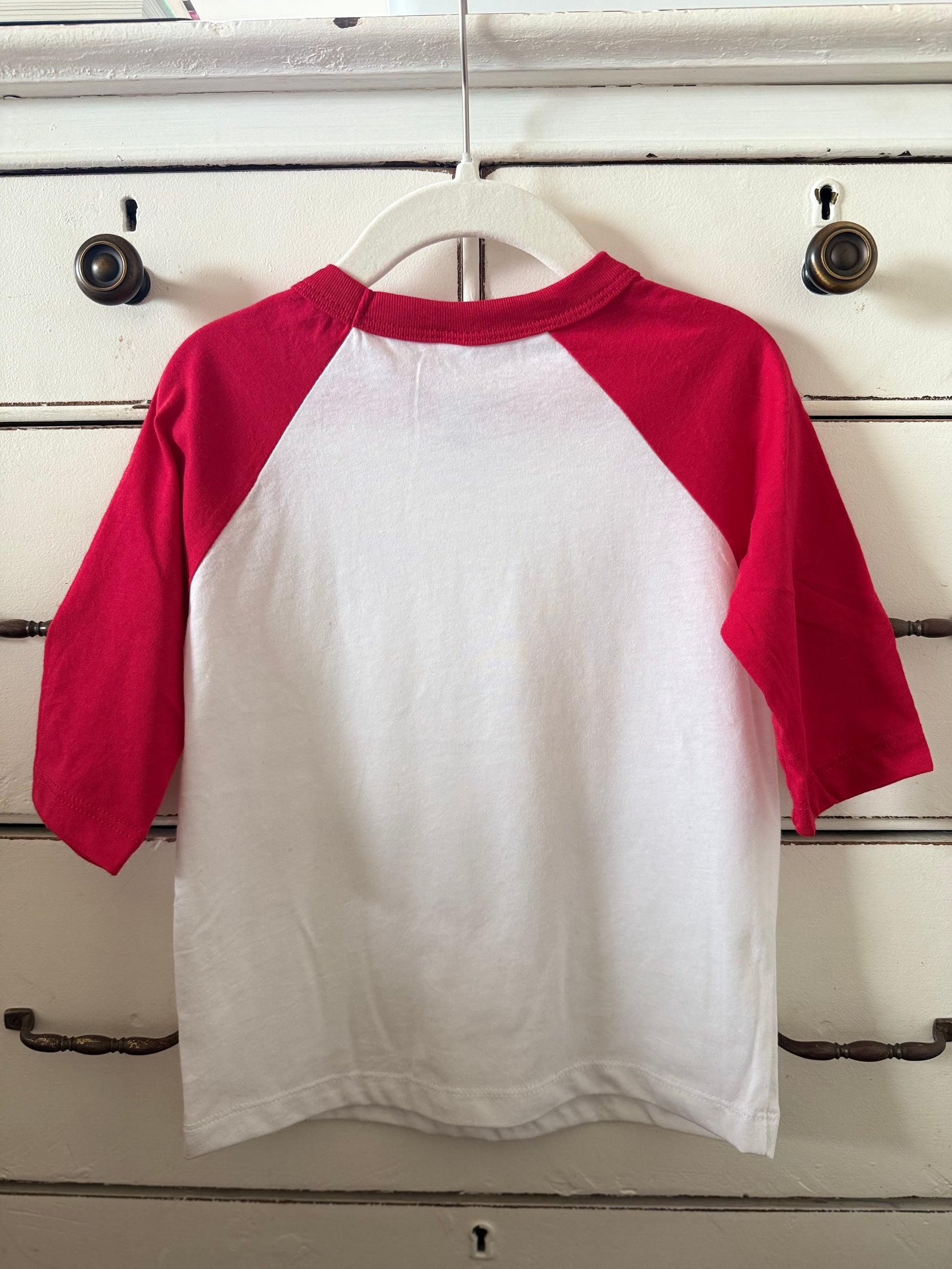 Red and white baseball shirt on a hanger against a wooden background