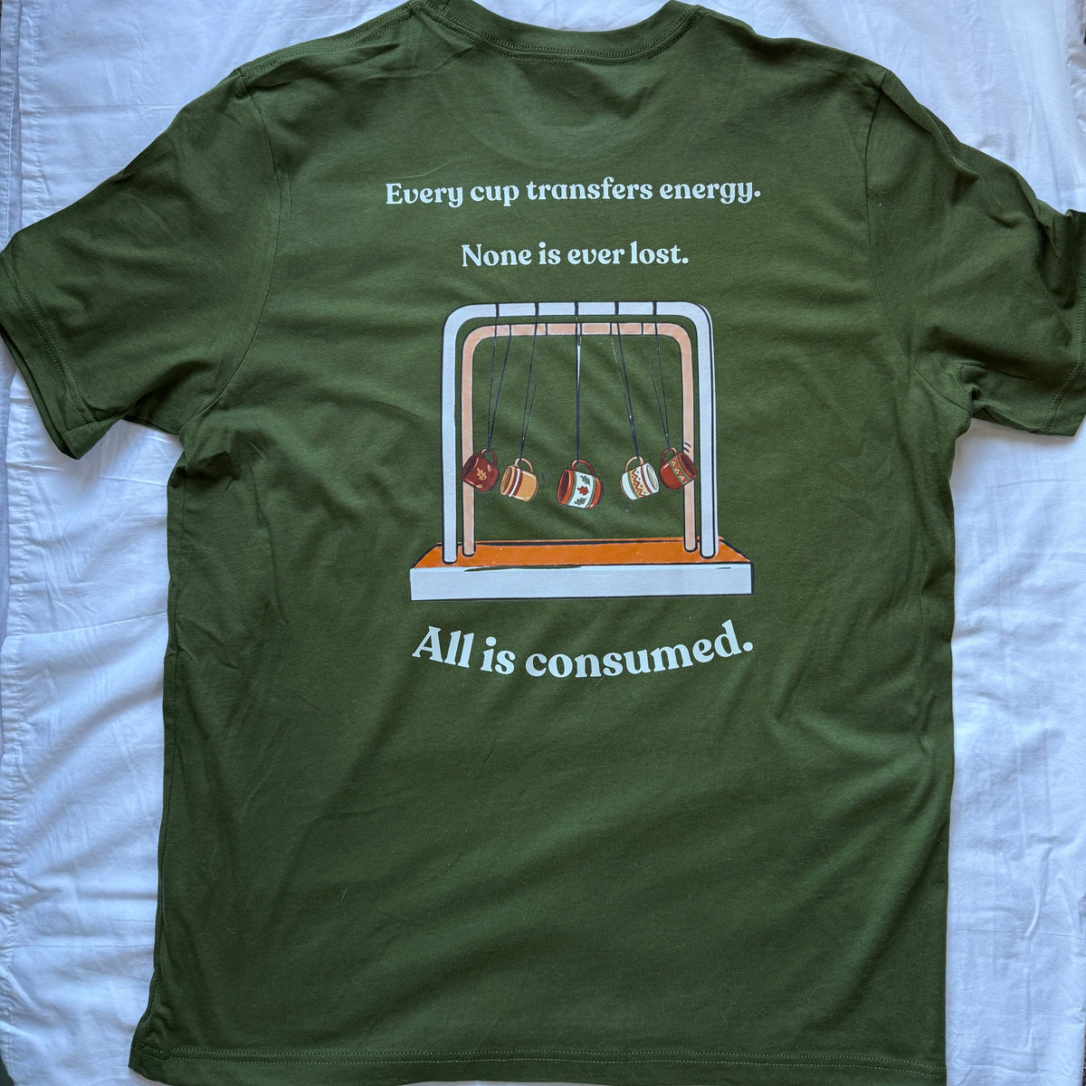 An olive green t-shirt laid flat on a white sheet, showing the back side with a printed graphic of a pendulum swing and the text 'Every cup transfers energy. None is ever lost.