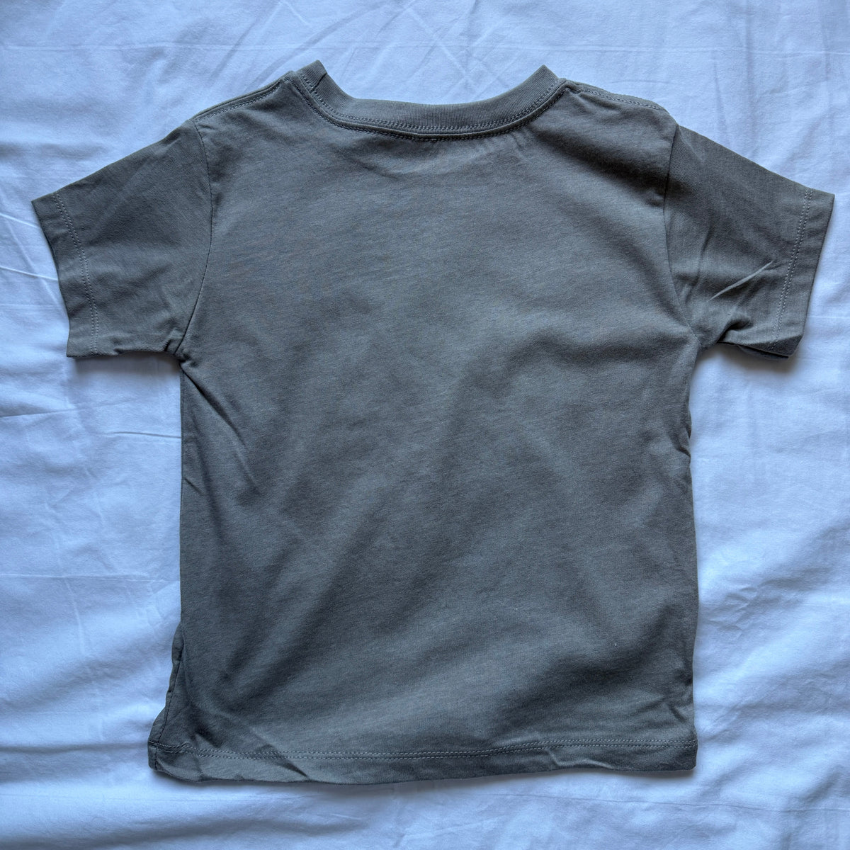 A dark gray short-sleeve t-shirt laid flat on a wrinkled light blue sheet.