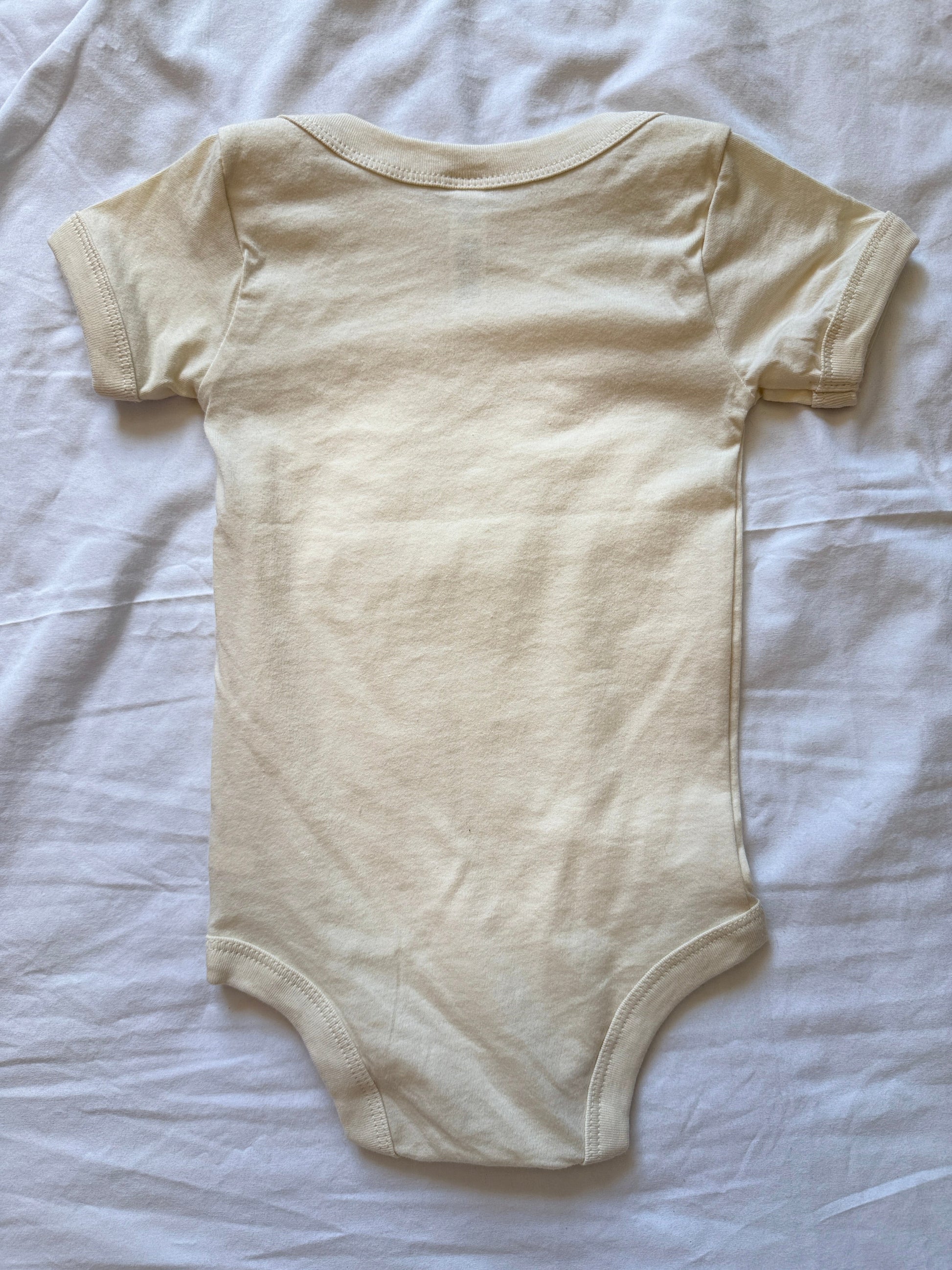 A light cream-colored short-sleeve baby bodysuit laid flat on a white fabric background.