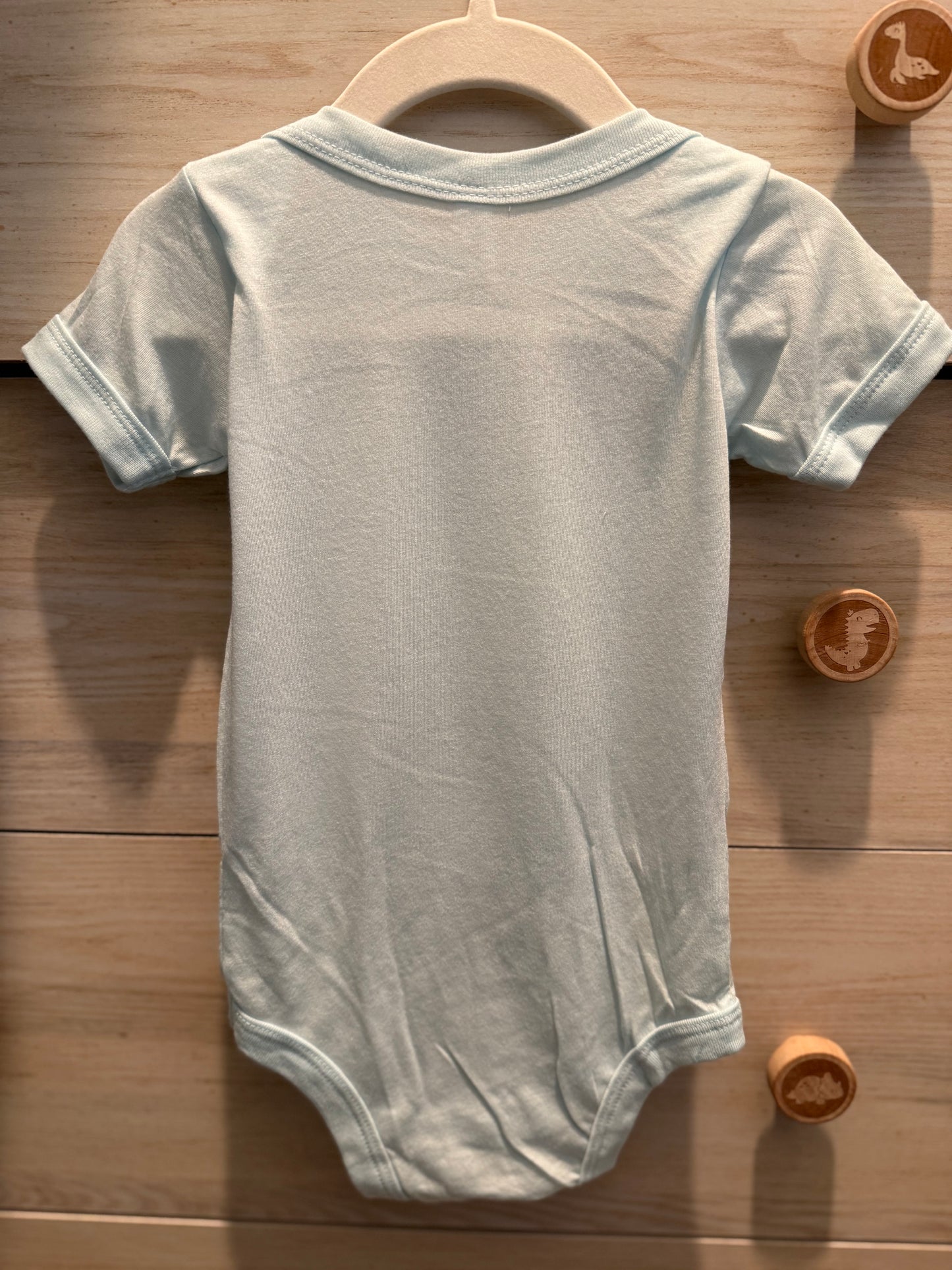 Gray baby onesie on a wooden hanger with wooden toys in the background