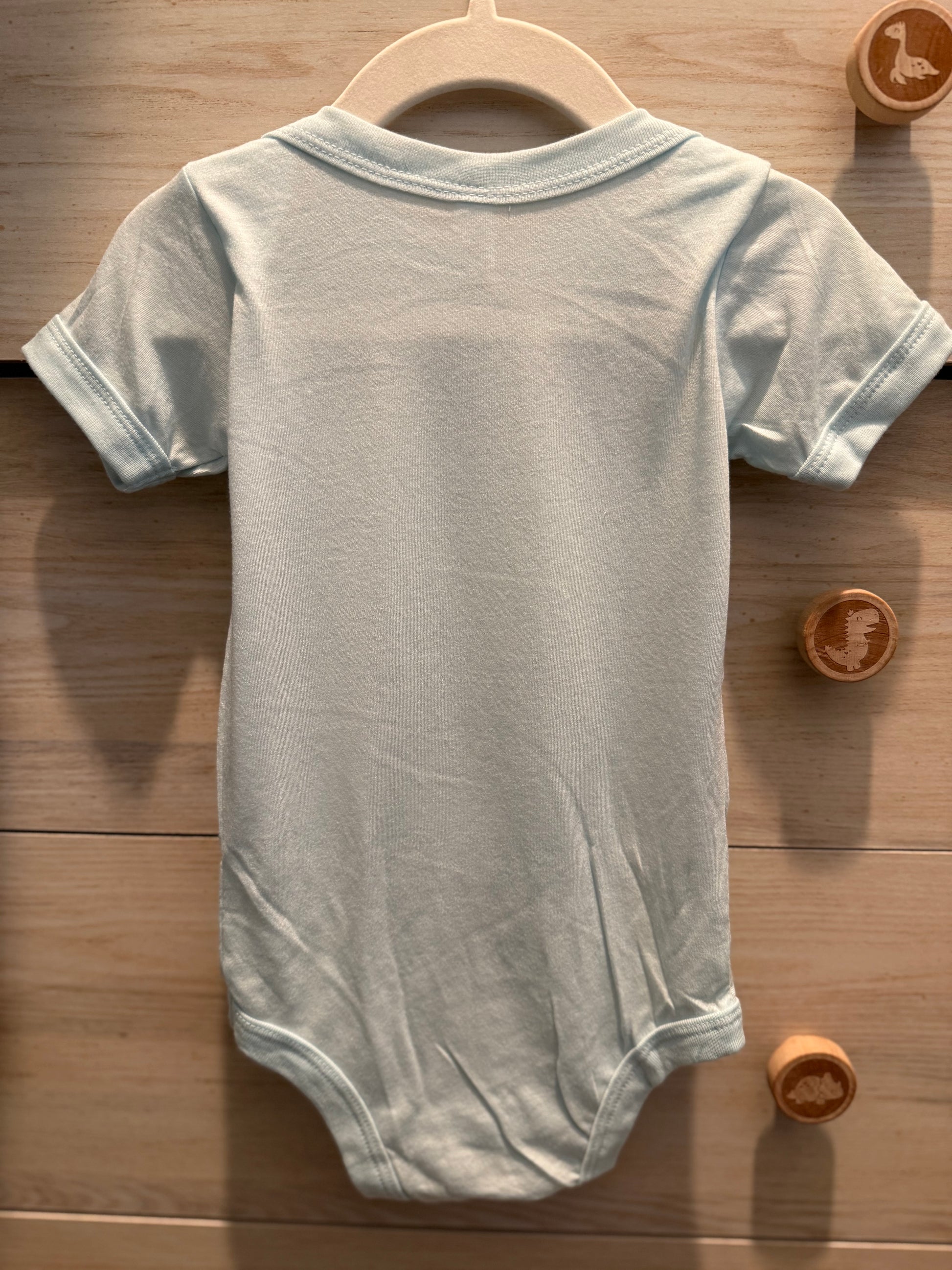 Gray baby onesie on a wooden hanger with wooden toys in the background