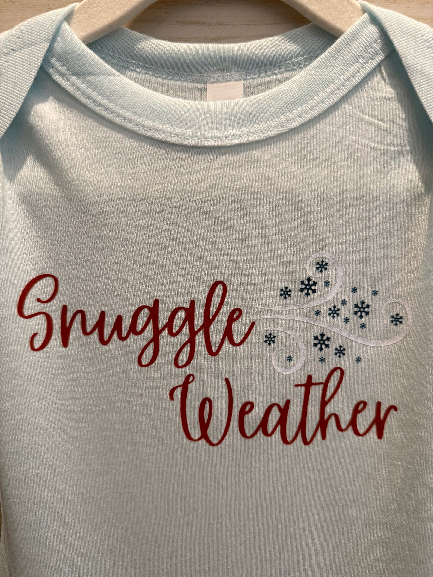 White baby onesie with 'Snuggle Weather' text and snowflake design.