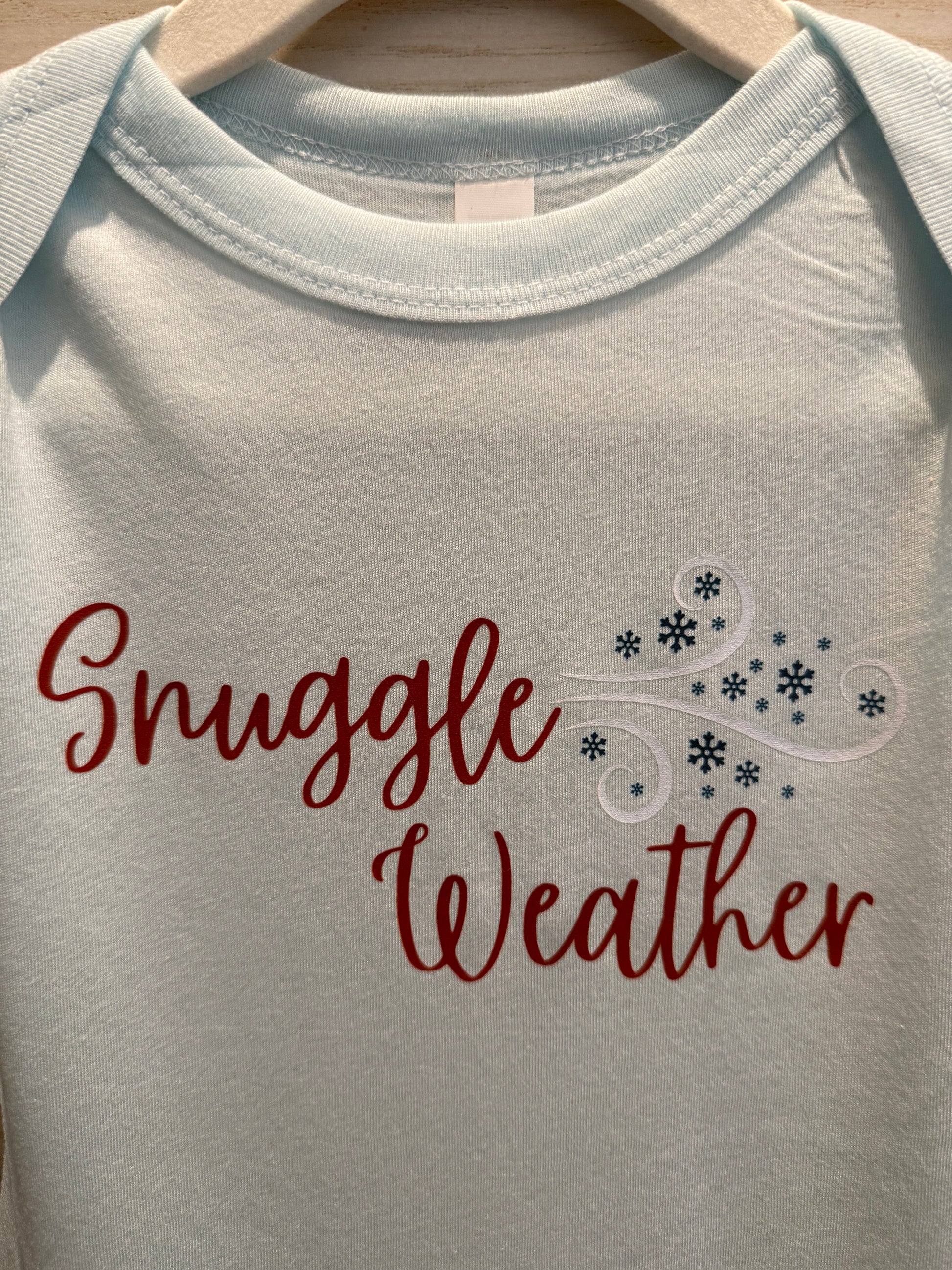 White baby onesie with 'Snuggle Weather' text and snowflake design.