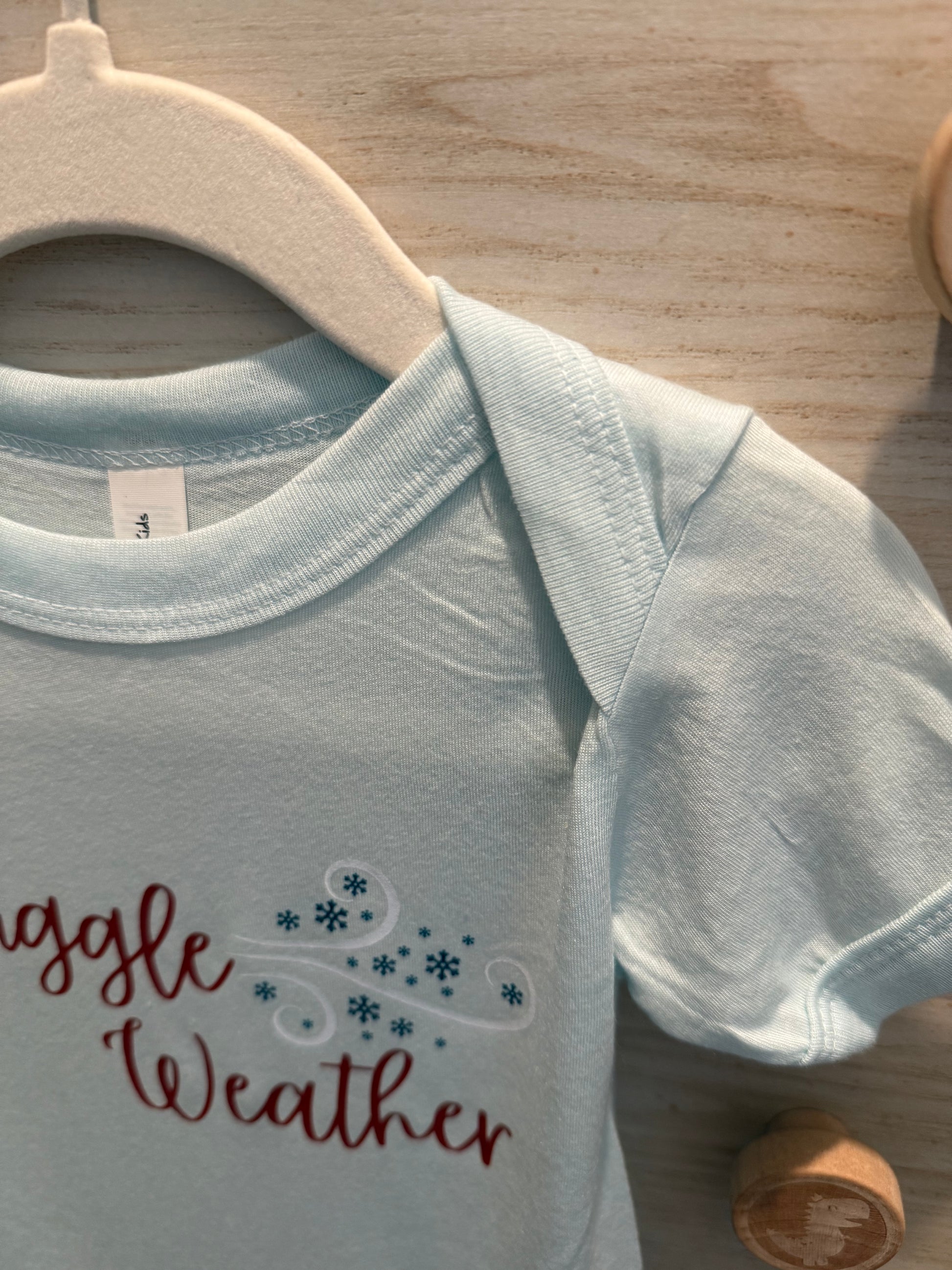 Light blue baby bib with 'Muggle Weather' text on a wooden surface