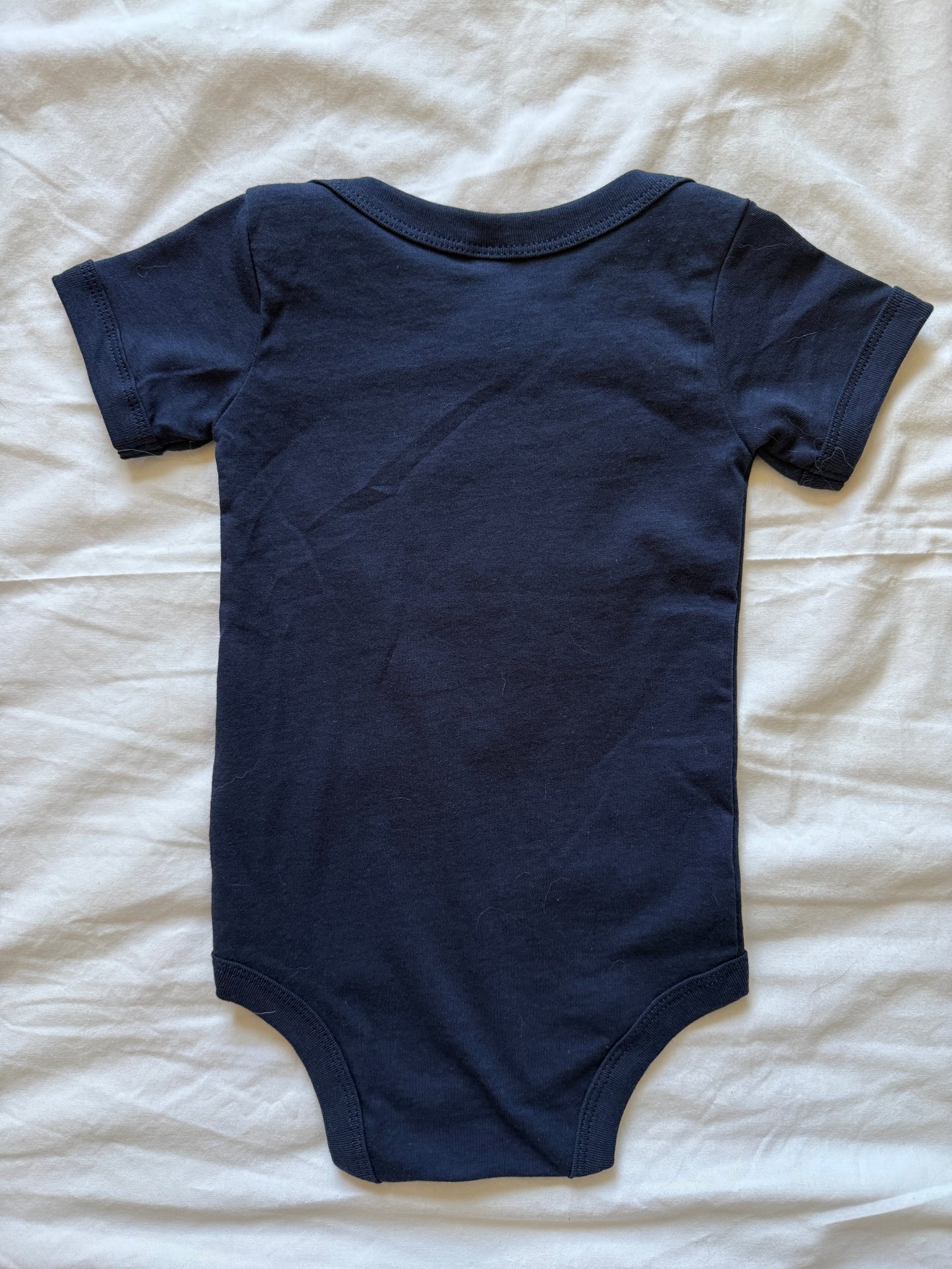 A navy blue short-sleeve baby bodysuit laid flat on a white fabric background.