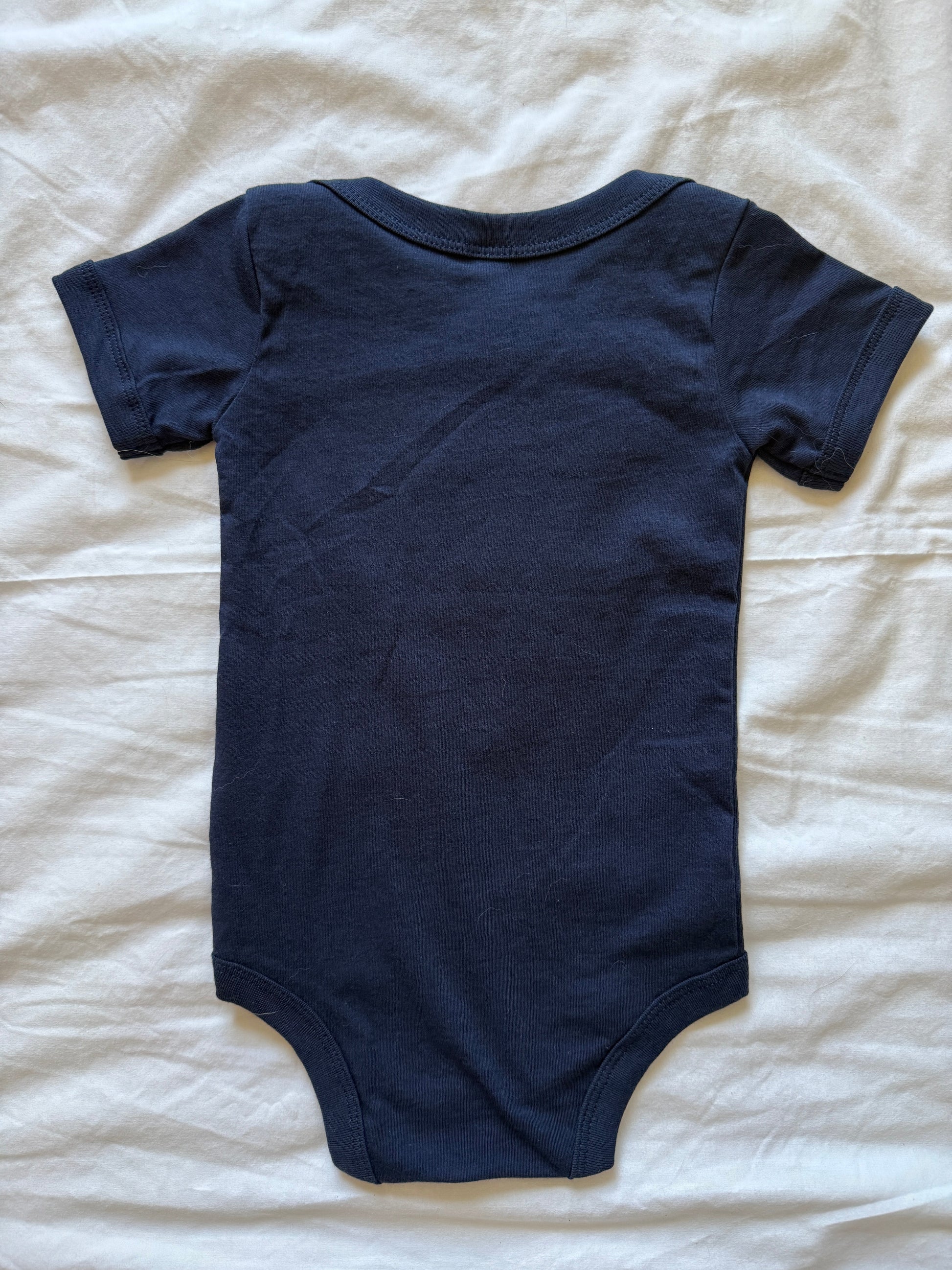 A navy blue short-sleeve baby bodysuit laid flat on a white fabric background.