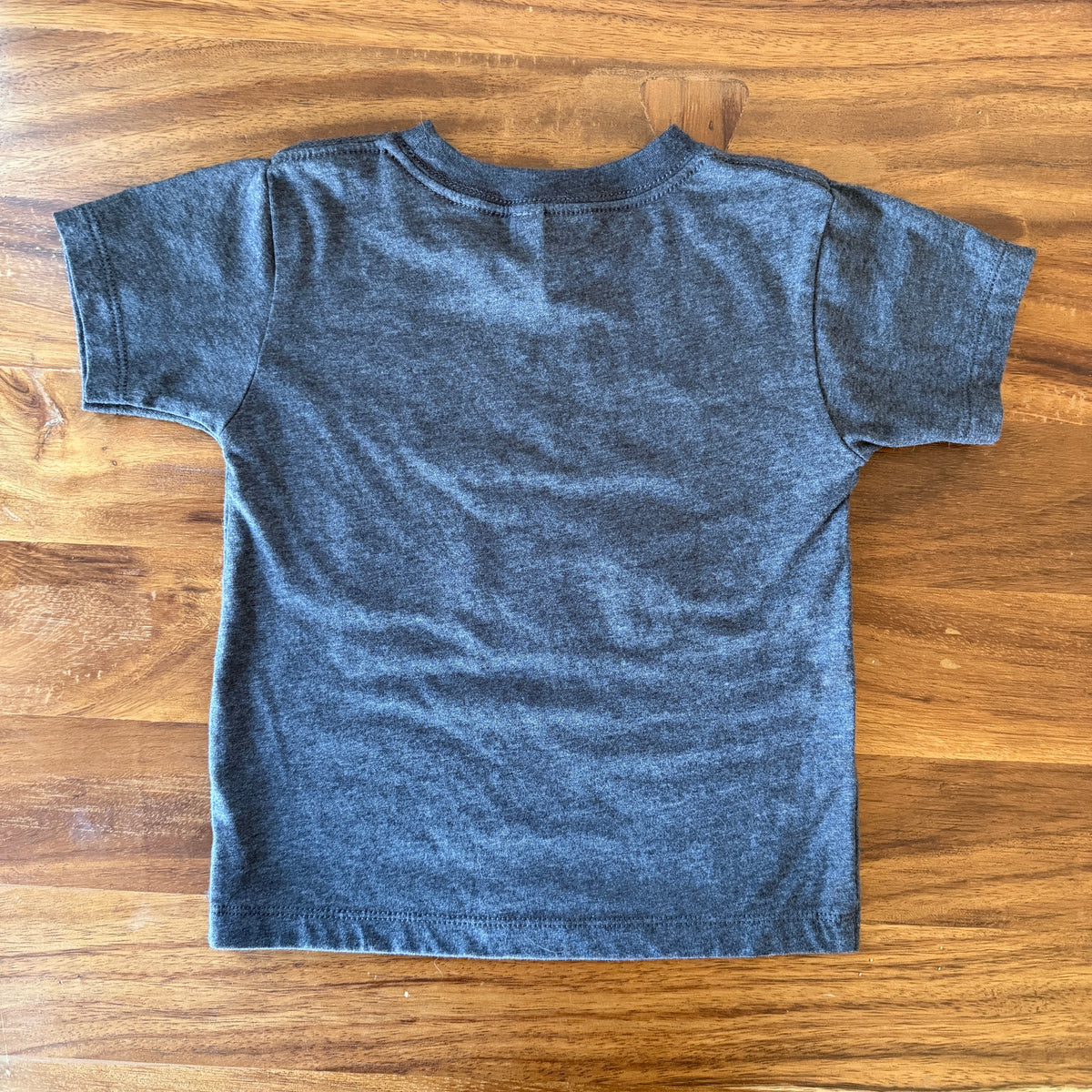 A dark heather gray short-sleeve t-shirt laid flat on a wooden table, viewed from the back.