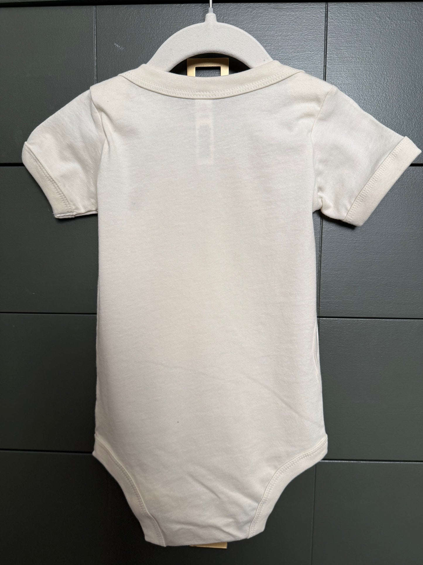 White baby bodysuit on a hanger against a gray tiled wall