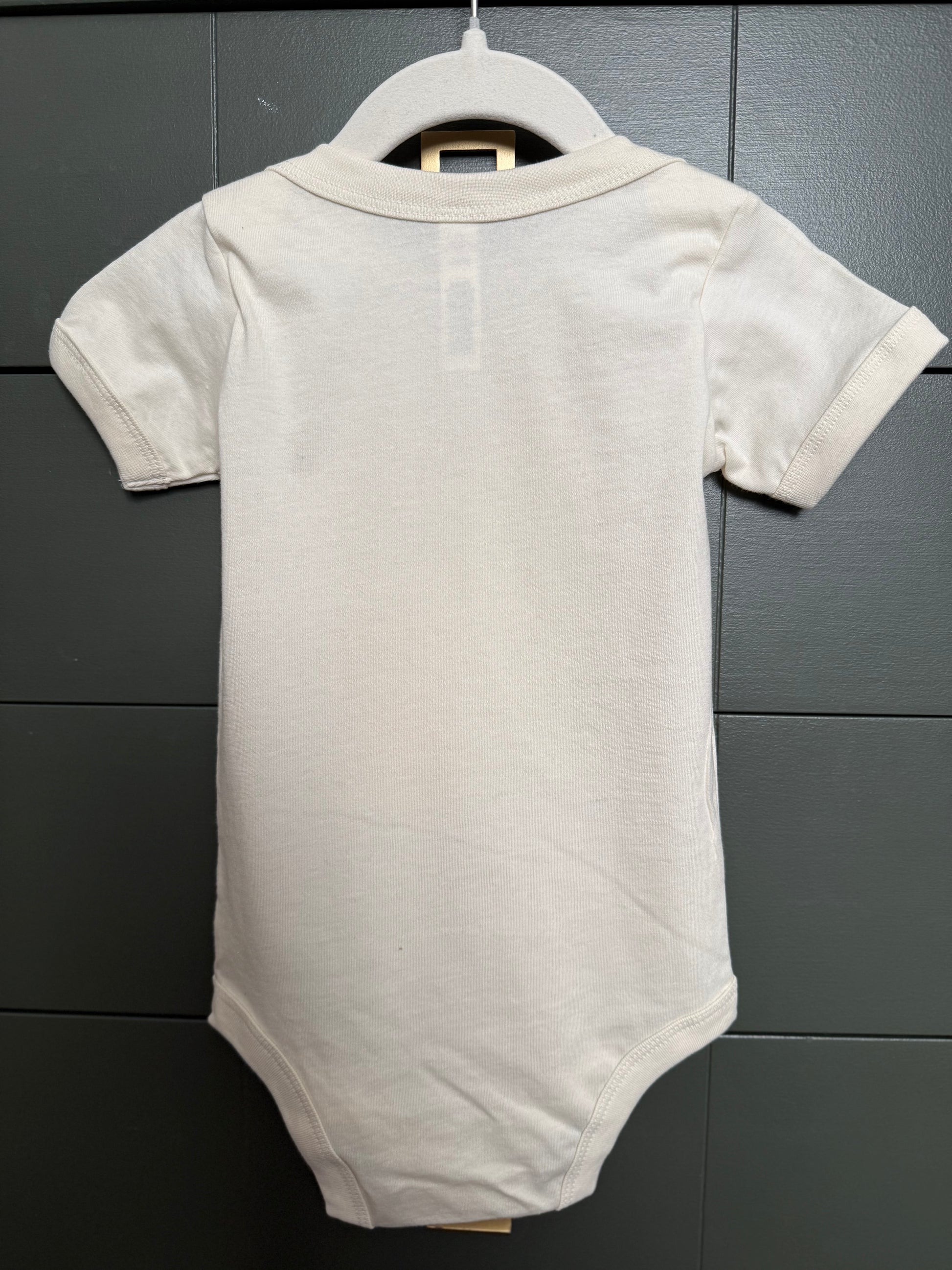 White baby bodysuit on a hanger against a gray tiled wall