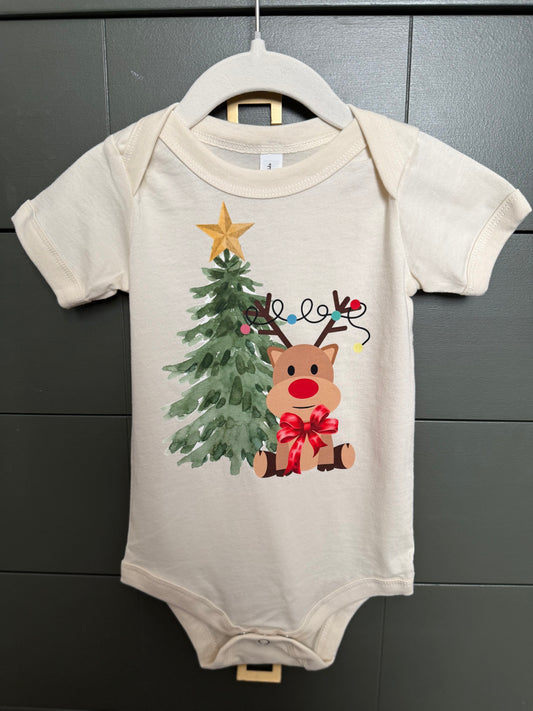 Baby onesie with Christmas tree and reindeer design on a hanger against a dark background