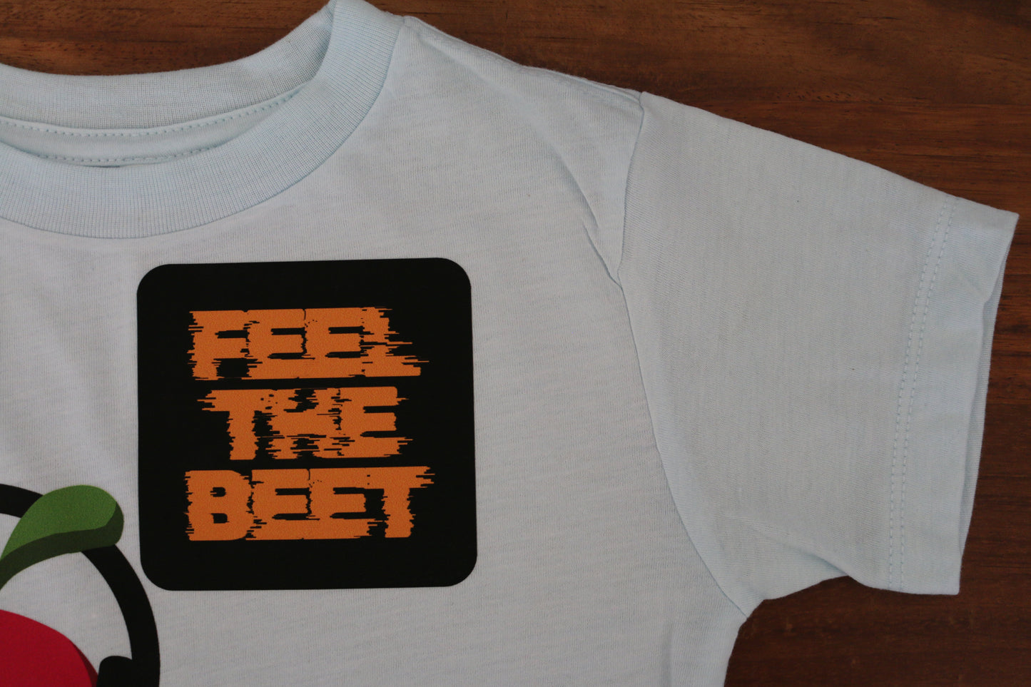White t-shirt with 'FEEL THE BEET' graphic on a wooden surface